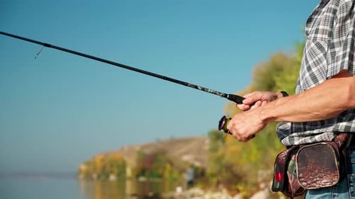 Die Hände eines reifen Mannes mit einer Angelrute beim Angeln auf dem Fluss