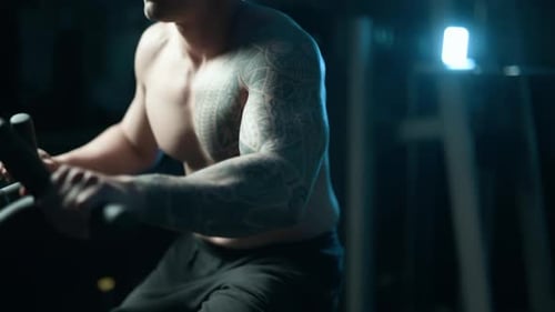 A Handsome Young Muscular Sportsman is Doing Exercise on a Fitness Machine in the Gym