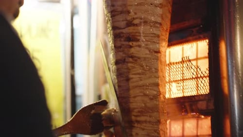 A large piece of chicken meat on a skewer for shawarma, A man cuts off the crust with a large knife