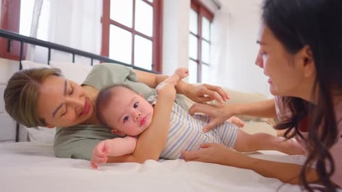 Asian lesbian couple lovingly caring for and raising their baby boy at home.