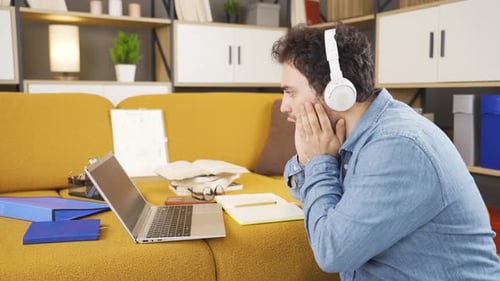 Man Works on Laptop at Home Wearing Headphones