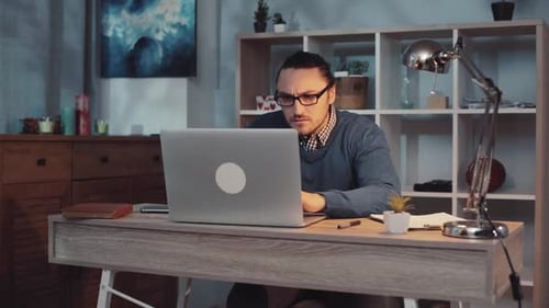Un jeune homme concentré qui travaille assidûment sur son ordinateur portable dans un espace de bureau à domicile moderne