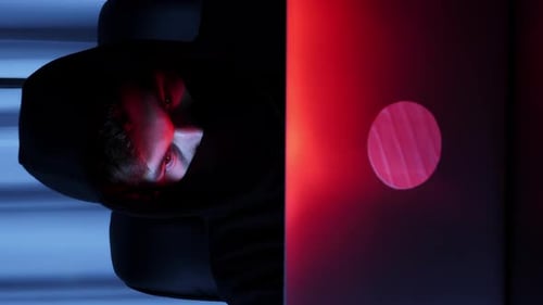 Gros plan d'un hacker masculin regardant l'écran d'un ordinateur portable assis dans une pièce sombre.