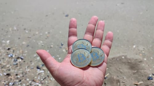 Homme tenant des pièces Bitcoin BTC sur fond de main, vagues de mer, plage de sable, bord de mer