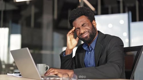 Stressed Businessman Suffering From Headache While Working on Laptop in Office