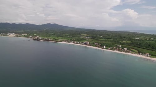 Drone moves forward, approaching the beach from the ocean, showcasing mountains and the coastline