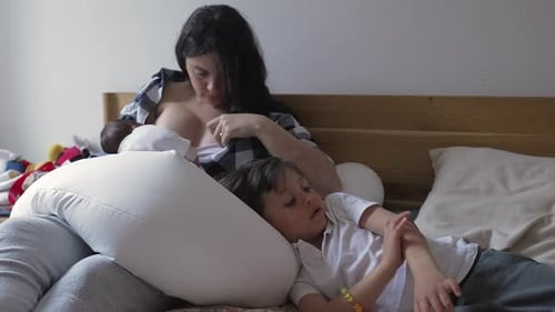 Mother Breastfeeding Infant with Child Lying Nearby