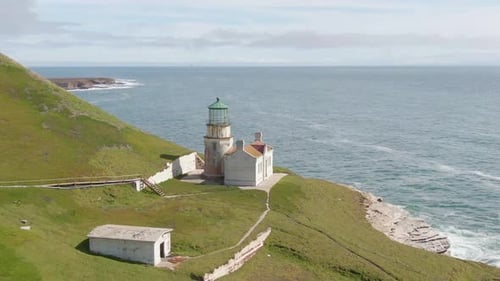Historic lighthouse on cliff side, aerial push in shot.