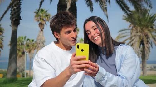 Happy Couple Looks at Phone on Tropical Beach