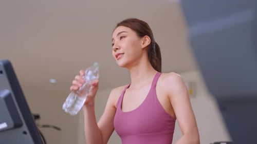 Asian young sportswoman drink a bottle of water while workout in gym.