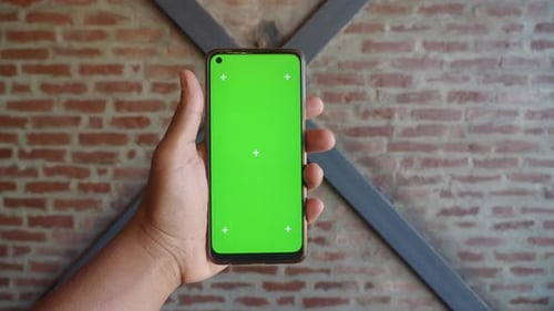 A Hand That is Holding a Smartphone with a Green Screen Intended for Mockups