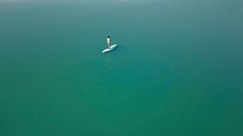 Aerial drone flying over a man doing stand up paddle in a blue water lake with mountains