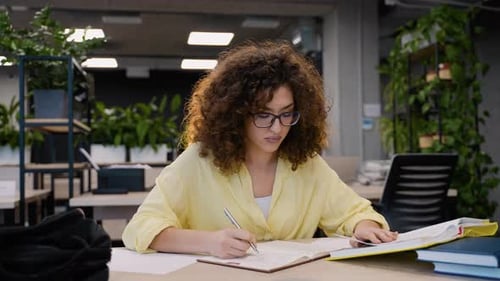Young Woman Studying and Writing at Library Desk