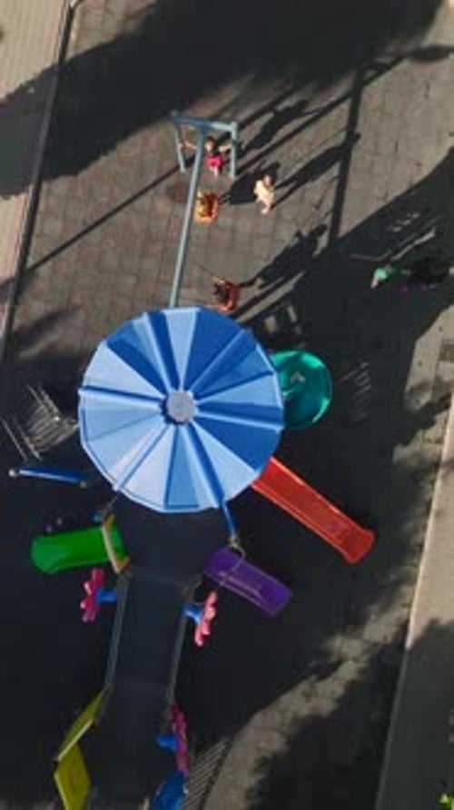 Vidéo verticale : enfants qui courent en riant sur une aire de jeux lumineuse avec balançoires, toboggans et cadres d'escalade