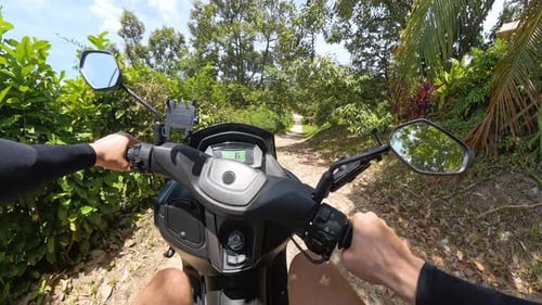 Homem andando de scooter em caminho de terra pela floresta tropical capturado do ângulo de primeira pessoa com Visible