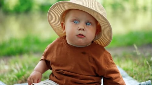 Lustiger kleiner Junge mit Mamas Hut sitzt draußen. Süßes Kind in der Natur im Sommer. Nahaufnahme.