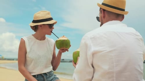 Young Woman Sipping Cocktail and Talking to Her Boyfriend on Beach
