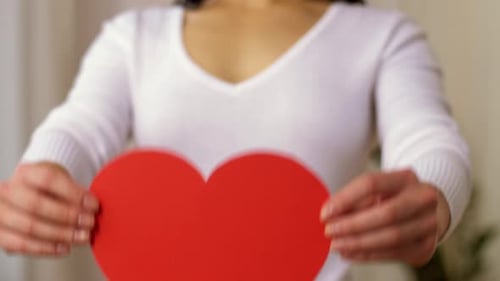 Woman holds red heart shape in front of her