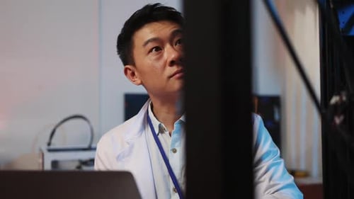 Japanese Focused Young Man with Laptop Learning 3d Printer Modeling New Plastic Component Inside