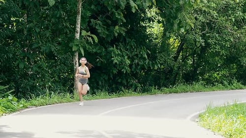 Young woman runner listening music on headphones while running on road in the morning.