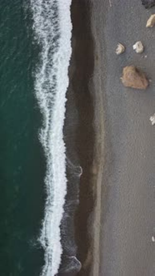 Aerial Vertical View of Beach with Wave Caressing Shore Sun Glare Small Waves on the Water Surface