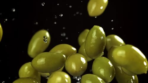 Delicious green olives falling with water on black background