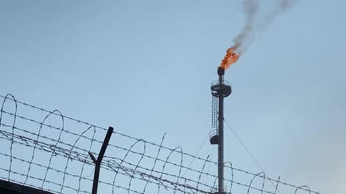 Telephoto close up of burning Gas Flare also known as flare stack, behind wall
