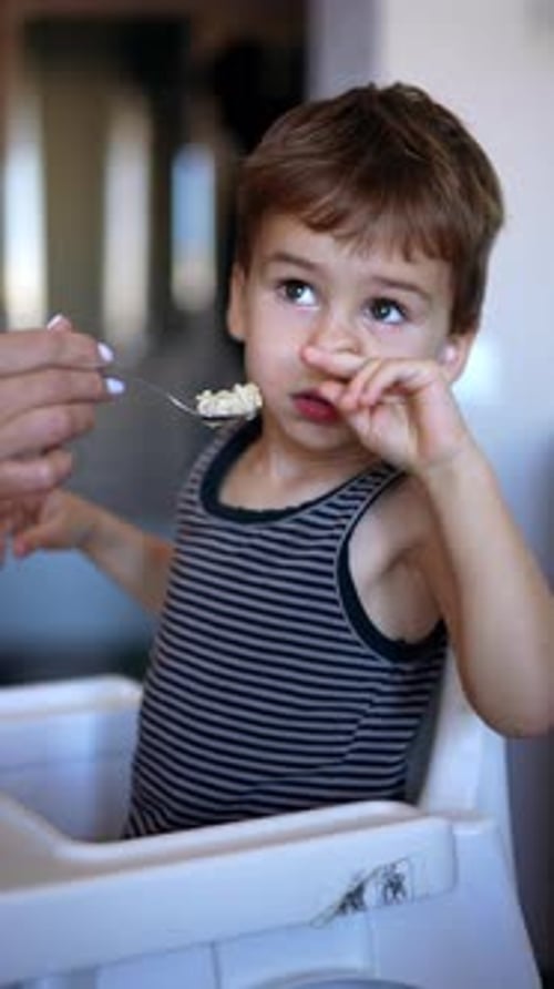 El
niño pequeño se niega a comer. Mamá le da gachas en la cuchara a su hijo, pero él se da la vuelta.