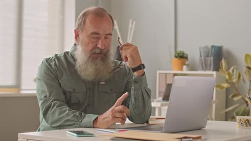 Senior Businessman Video Chatting with Team on Laptop in Office