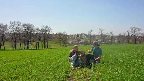 People Kneeling in Field Petting Labrador Dog
