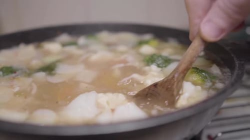 Moving mixing and stirring Chopped Vegetables cooking in broth with wooden spoon authentic recipe ru