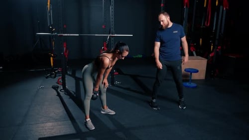beautiful young fitness woman doing exercises with dumbbells in hands with trainer in gym preparing