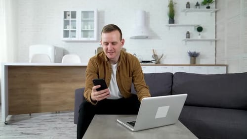 Young Adult Using Phone and Laptop at Home