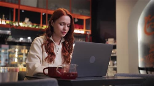 Side Camera View of Woman Sitting Alone in Cozy Cafe While Focusing on Laptop Screen Working