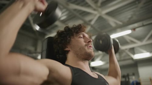 Muscular Man Lifting Dumbbells Overhead during Shoulder Workout in Gym