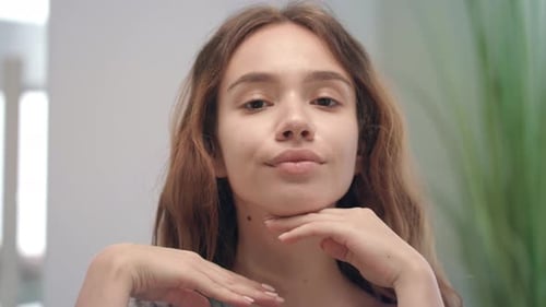 Young Woman Doing Skin Massage on Face and Chin at Mirror In