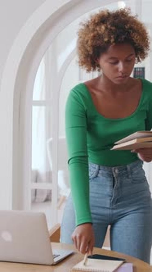 Woman Reading Book and Using Laptop at Home