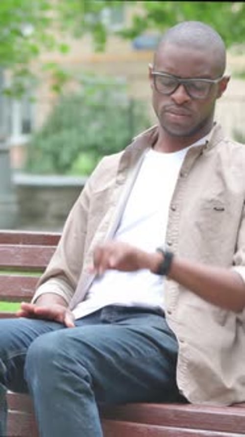Vertical Video, Waiting Young African Man Checking Wrist Watch on Park Bench