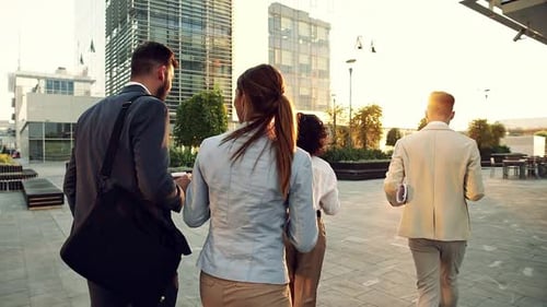 Group of coworkers walking outside in front of office buildings discuss about business plan.