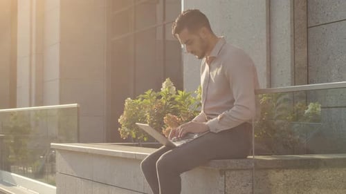 Young Adult Working on Laptop Outside Office Building