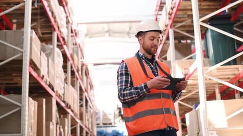 Holding tablet. Storage worker in uniform is in the warehouse