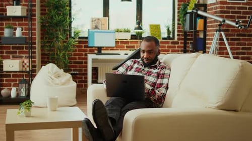 Man Relaxing on Couch Using Laptop Indoors