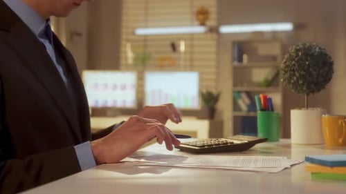 Side View of a Man Counting on a Calculator and Writing the Data Into a Report