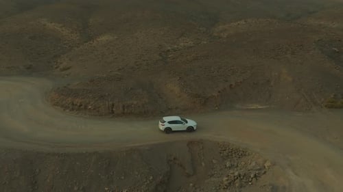 Fantastic aerial view with tracking of a white car driving along a winding dirt road in a desert and