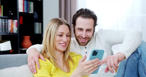 Close Up of the Happy Cheerful Young Caucasian Couple Sitting on Couch in Living Room and Using