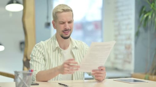 Young Adult Man Frustrated With Paperwork at Desk