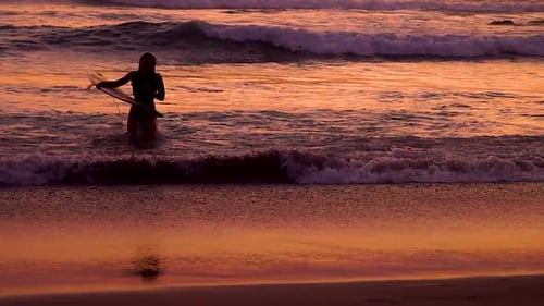 Silueta de una mujer surfista saliendo del agua en cámara lenta. Las olas se rompen maravillosamente