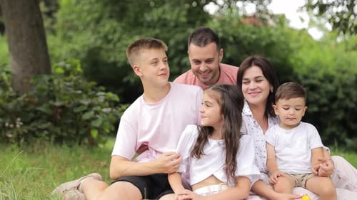 Happy Young Family Dad Mom and Three Children Laughing Sitting in a Meadow on the Grass in the Park