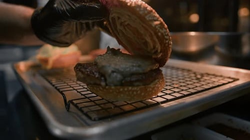 Burger cooking process - chef adding ingredients to bun in restaurant kitchen
