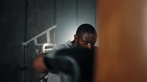 Boxer Training Hitting Punching Bag African American Sweated Sportsman Practicing Punches in Gym